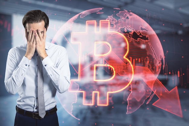 businessman covering face with hands next to falling global red bitcoin hologram