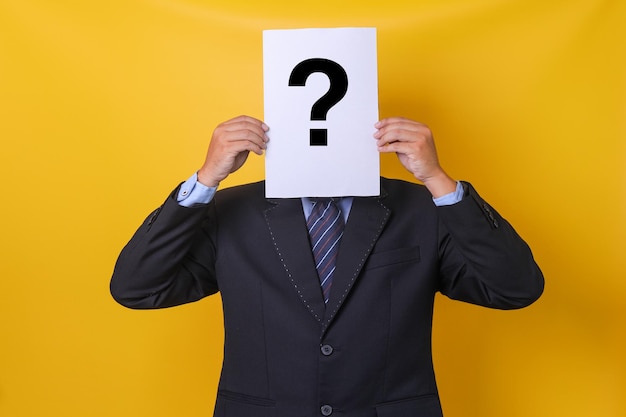 Businessman covering his face with a white paper with big question mark symbol Doubtful man holding