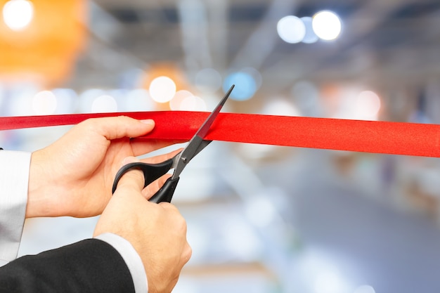 Businessman cutting red ribbon with pair of scissors