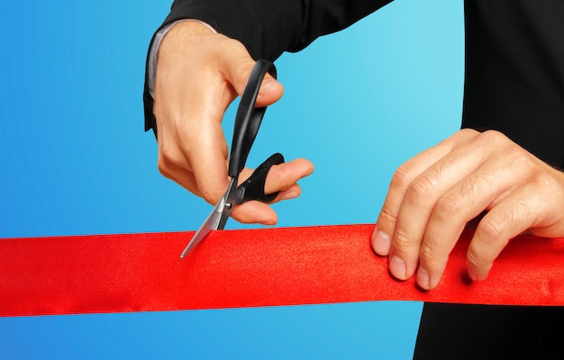 Photo businessman cutting red ribbon with pair of scissors