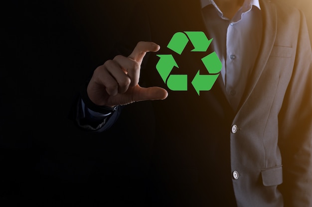 Businessman over dark background holds an recycling icon,sign in his hands.Ecology,environment