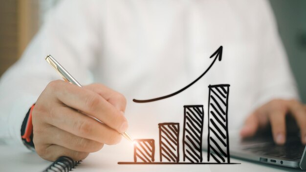 Businessman draws an increasing trend arrow and a rising chart from plan to goal It is a representation of the idea of corporate investment development