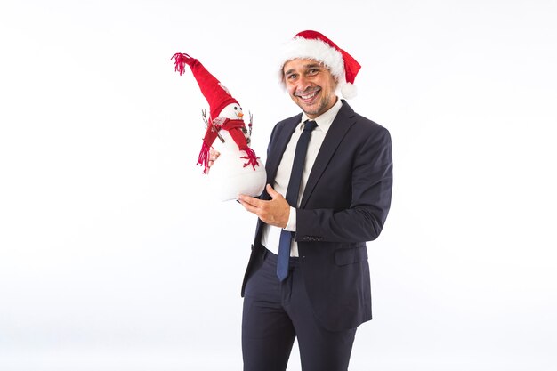 Businessman dressed in suit, tie and Christmas hat of Santa Claus, smiling with a snowman, on white background. Christmas celebration concept.