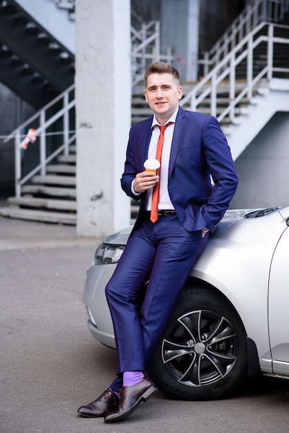 Businessman drinking coffee near the car.