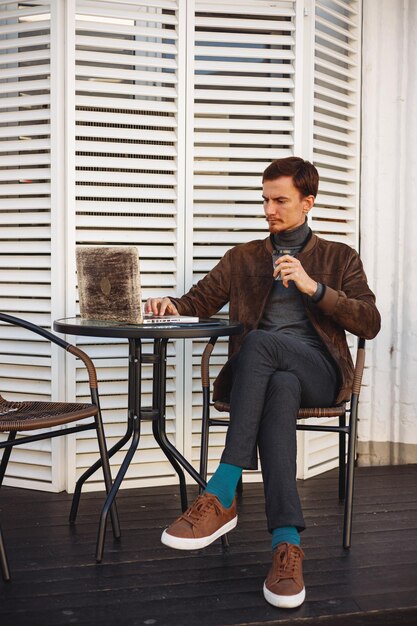 Businessman drinking coffee and working on laptop while sitting at table in street cafe