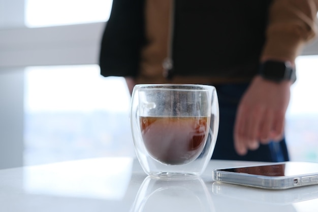 Businessman drinking coffeetransparent cup of coffee on white marble desk having break deep in thoughts enjoying view waiting for meeting to start making business decision