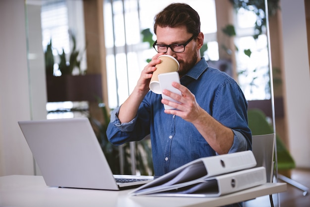 Businessman drinking office while using cellphone at creative office