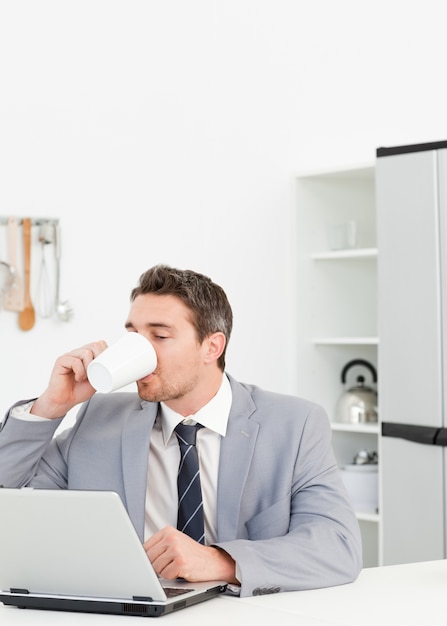 Businessman drinking while he is looking at his laptop