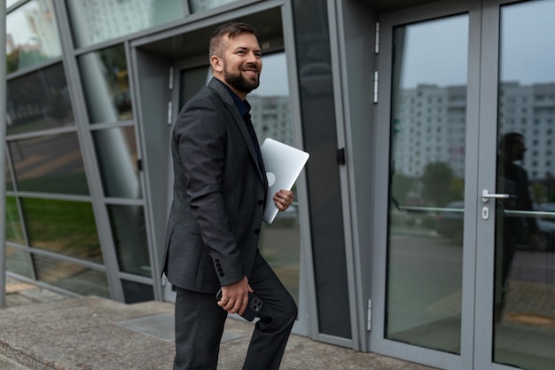 A businessman enters the building with a laptop in his hands and a mobile phone with a smile looking