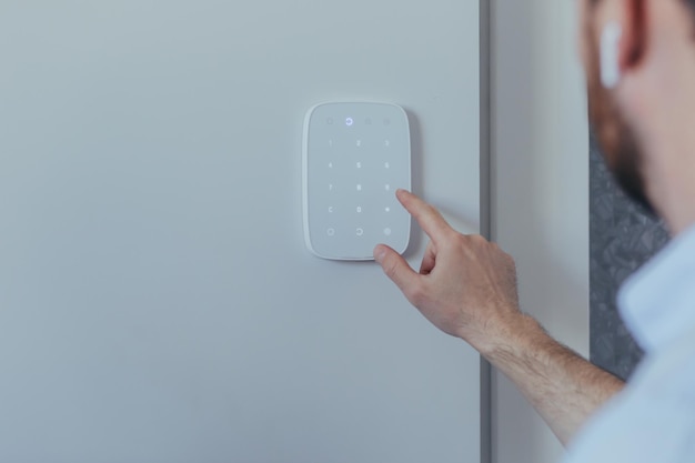 Businessman enters finger password lock code on alarm panel on white wall rear view of man with beard