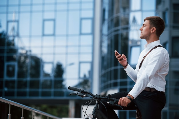 Businessman in formal clothes with black bicycle is in the city.