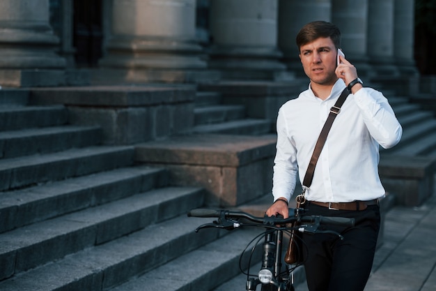 Businessman in formal clothes with black bicycle is in the city.