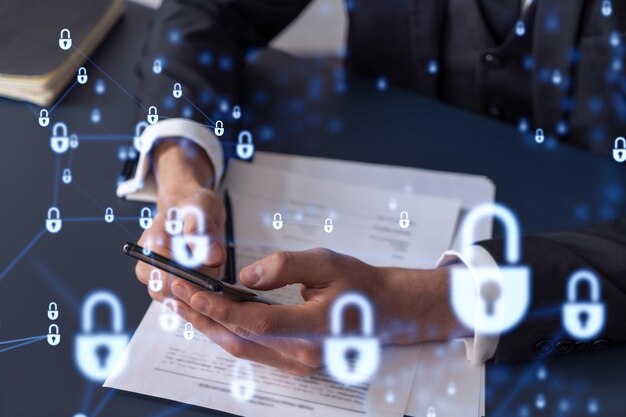 A businessman in formal wear reading the contract to prevent\
probability of risks in cyber security and checking details in the\
phone padlock hologram icons over the working desk