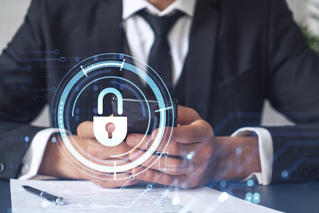 A businessman in formal wear reading the contract to prevent\
probability of risks in cyber security and checking details in the\
phone padlock hologram icons over the working desk