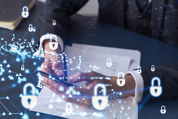 A businessman in formal wear reading the contract to prevent probability of risks in cyber security and checking details in the phone Padlock Hologram icons over the working desk