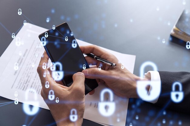 A businessman in formal wear reading the contract to prevent probability of risks in cyber security and checking details in the phone Padlock Hologram icons over the working desk