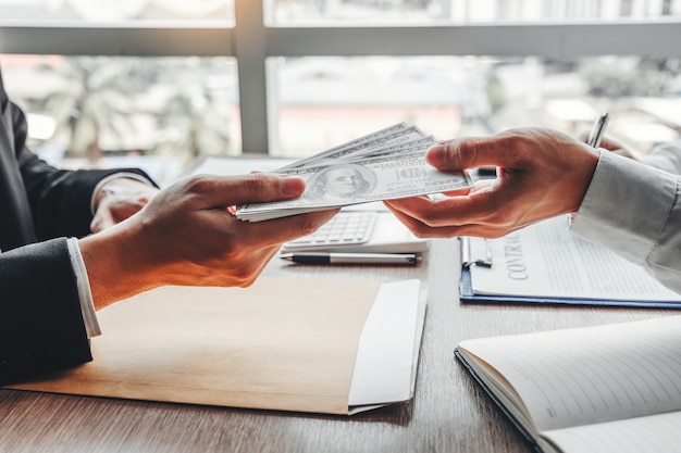 ,Businessman giving dollar bills to business manager to deal contract