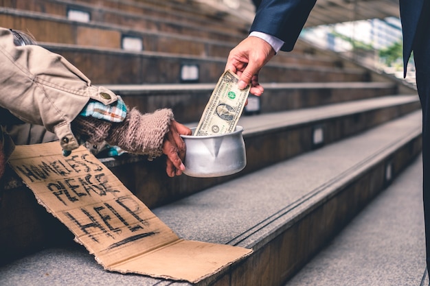 Businessman giving donation dollar cash with sleeping old homeless person