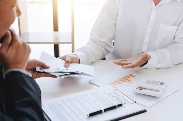 Businessman giving money in the envelope while making deal to agreement a real estate