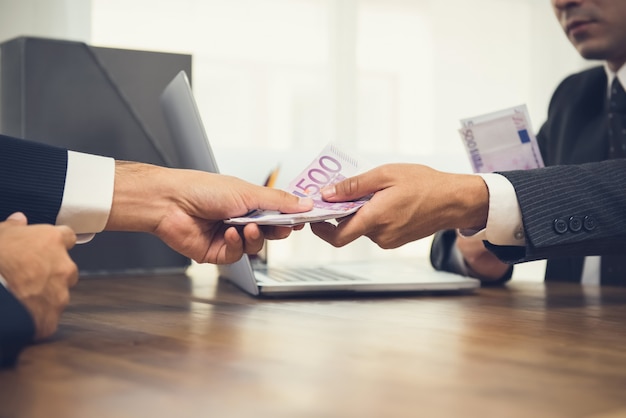 Businessman giving money, Euro banknotes, to his partner on working desk