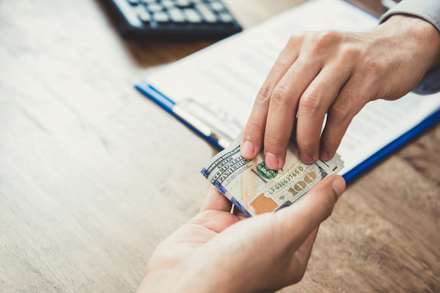 Businessman giving money, US dollars, to his partner while making contract