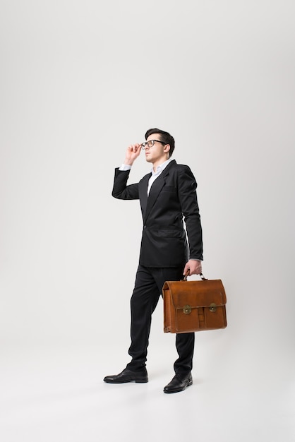 Businessman in glasses and black suit holds brown leather briefcase in hand isolated on white