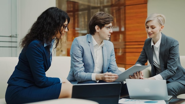 Businessman in glasses talking with female business partners sitting on couch in meeting room