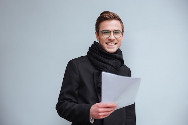 Businessman in glasses and warm clothes looking at documents and standing near the wall