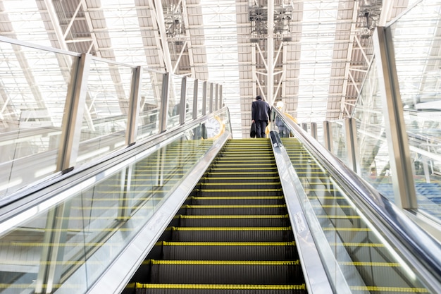 Businessman going up an escalator with luggage