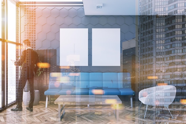 Businessman in a gray honeycomb wall pattern office lounge with loft windows, a coffee table, a sofa and a white armchair. Two vertical posters. 3d rendering mock up toned image double exposure