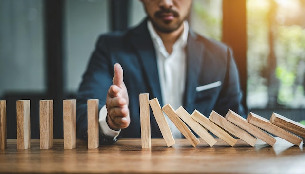 Photo businessman halts falling domino with hand symbolic of control and preventing chain reaction