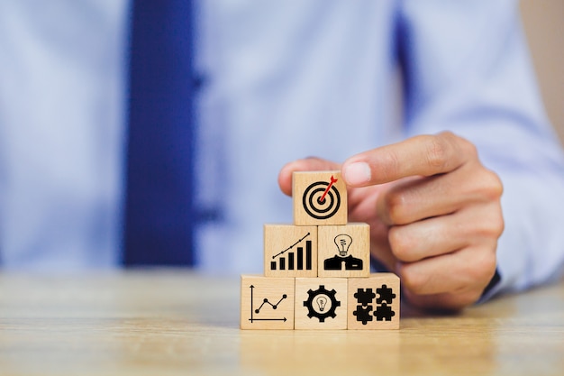 Businessman hand arranging wood block with icon target business strategy.