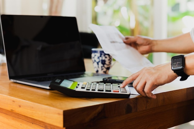 Businessman hand on calculator to calculate financial report and laptop computer on table