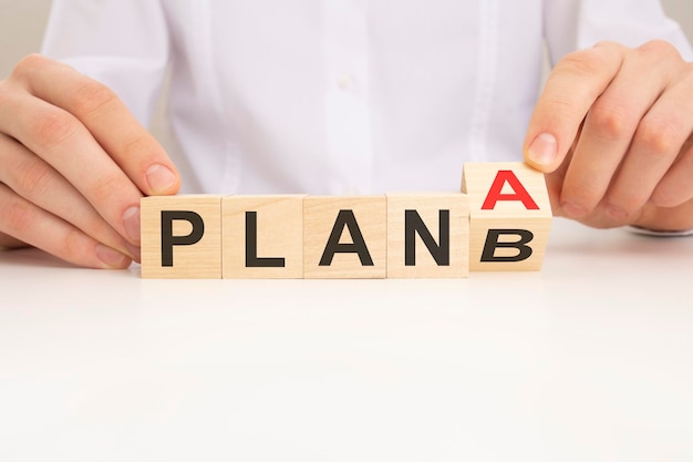 사업가는 테이블 배경 전략 분석 마케팅 프로젝트 및 위기 개념에서 PLAN A를 PLAN B 텍스트로 변경하여 나무 큐브 블록을 뒤집습니다.