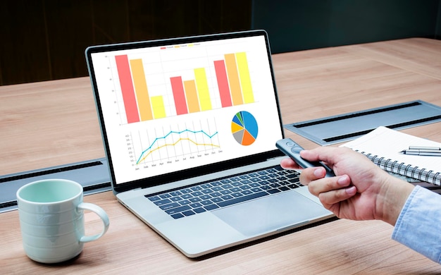 Businessman hand hold remote control slide with mock up chart\
presentation on display laptop
