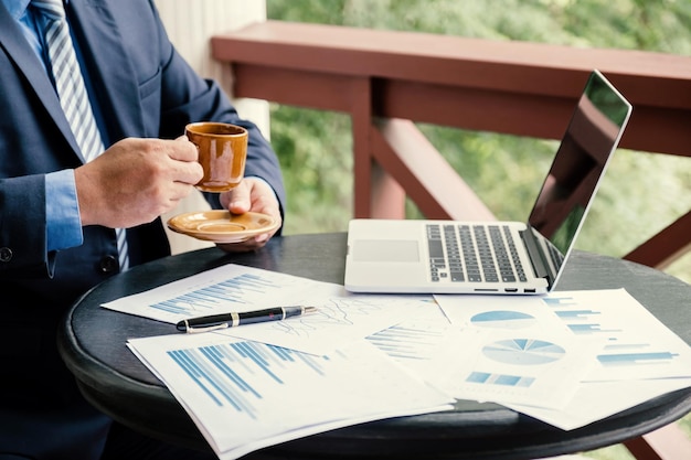 Businessman hand holding coffee cup analysis the graph with laptop at the home office for setting challenging business goals And planning to achieve the new target