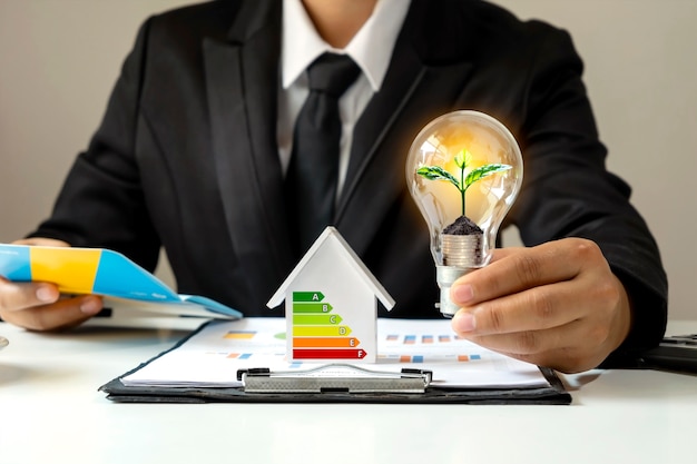 Businessman hand holding energy-saving light bulb with plants growing on coins in light bulbs