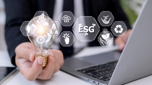 仮想画面に esg アイコンが付いた電球を持っているビジネスマンの手 ESG 環境社会および企業統治の概念