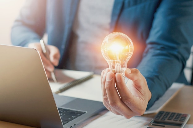 businessman hand holding lightbulb with working accounting in office