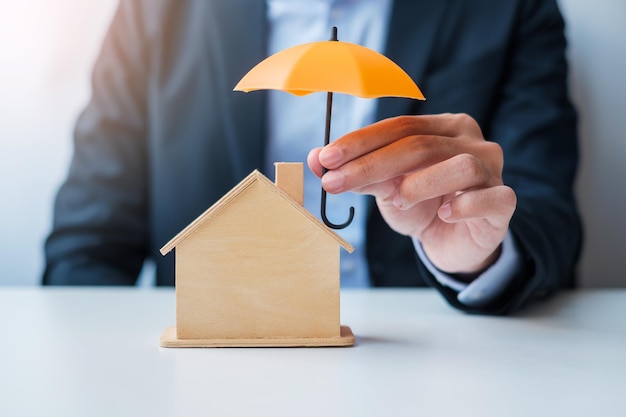 Businessman hand holding orange Umbrella cover wooden Home model real estate insurance and property concepts