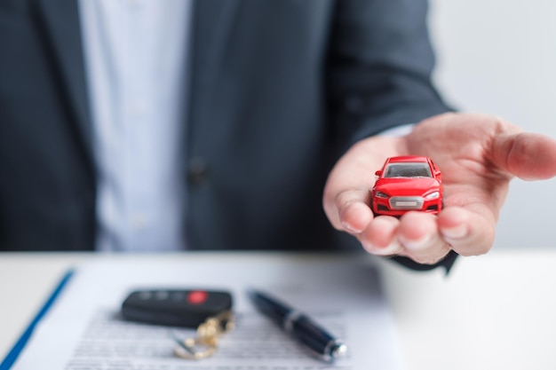 Businessman hand holding red car toy with vehicle keyless pen and contract document buy and sale insurance rental and contract agreement concepts