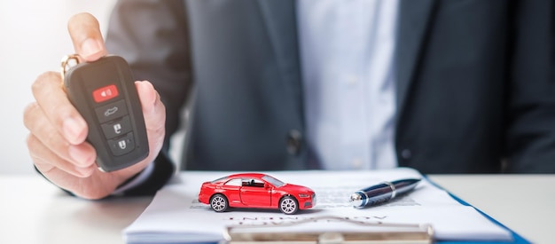 Businessman hand holding remote keyless with car toy pen and contract document buy and sale insurance rental and contract agreement concepts