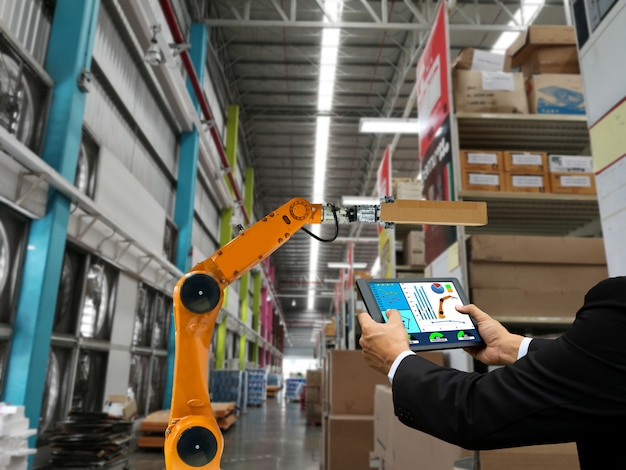 Businessman hand holding a tablet smart robot industry arm products storage factory and warehouse