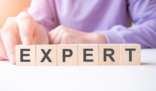 손으로 나무 큐브 블록을 들고 있는 사업가, 테이블 배경에 EXPERT 사업 단어, 미션, 비전, 핵심 가치 개념