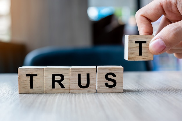 Businessman hand holding wooden cube block with TRUST business word on table background.