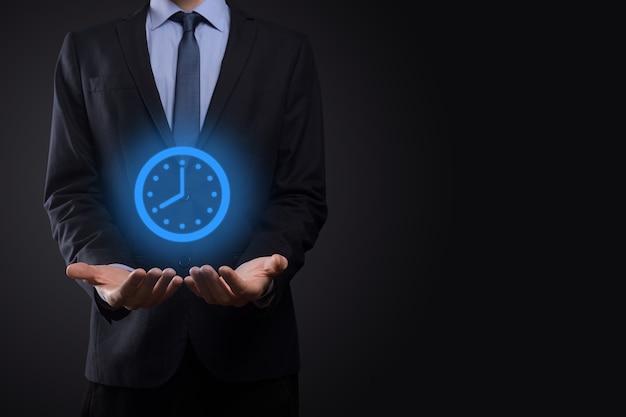 Businessman hand holds the icon of hours clock with arrow.