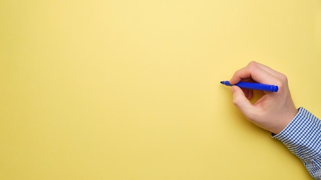 Businessman Hand holds a pencil on a yellow sheet of paper with a top view and copy space.