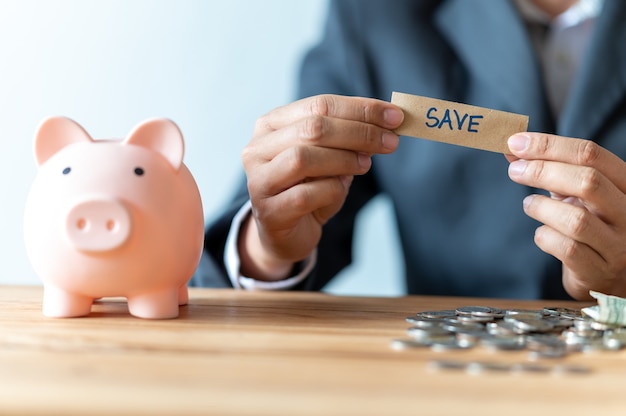 Businessman hand inserting a coin into a piggy bank for business and save money