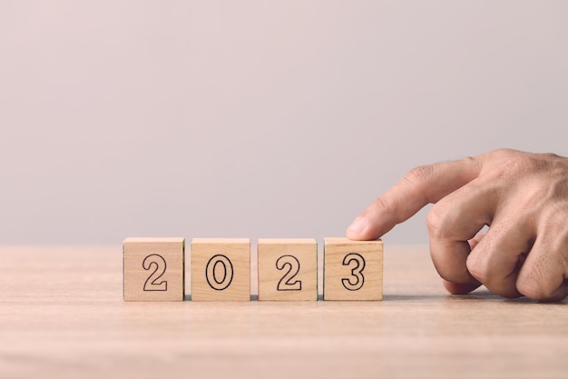 Businessman hand is sorting out a wooden dice with the number of 2023 on the table Work concept in