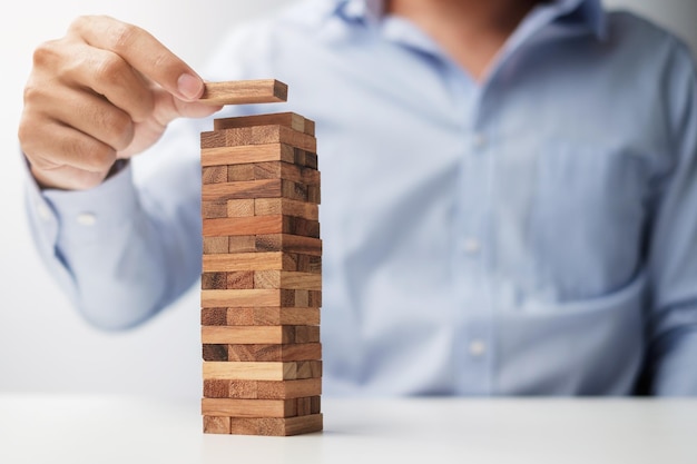タワーに木製のブロックを配置または引っ張るビジネスマンの手ビジネス計画リスク管理ソリューションと戦略の概念